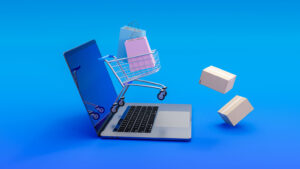 Laptop con carrito de compras pequeño y bolsas aisladas sobre fondo azul, simbolizando el comercio electrónico y la transformación digital de los negocios